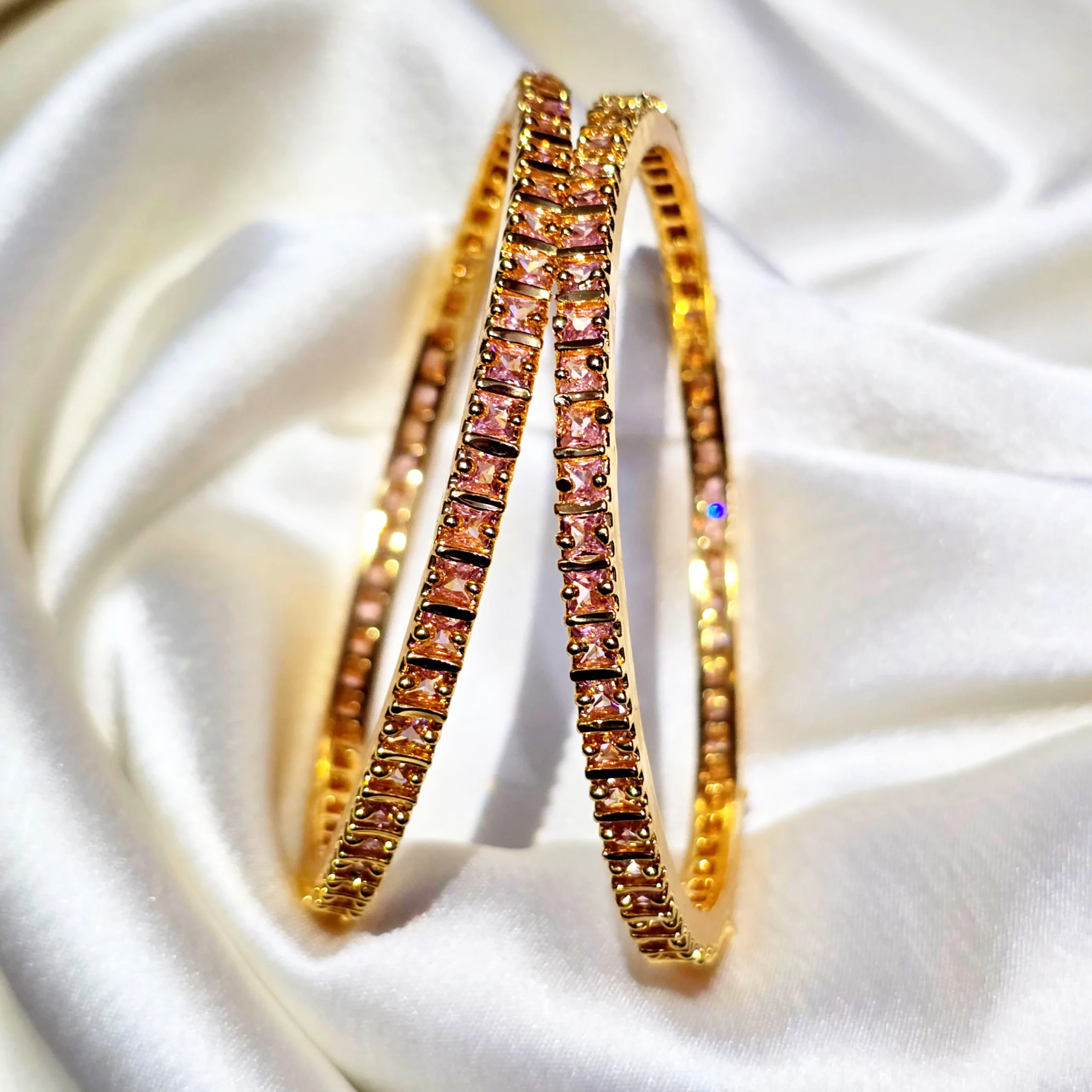 Gold-plated pink stone bangles displayed on white satin fabric