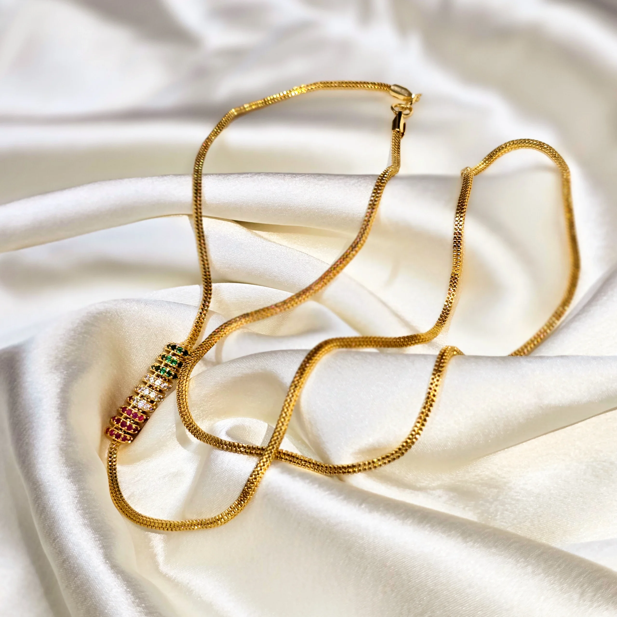 Gold-plated minimal chain necklace with multicolor stone bar pendant on white satin fabric