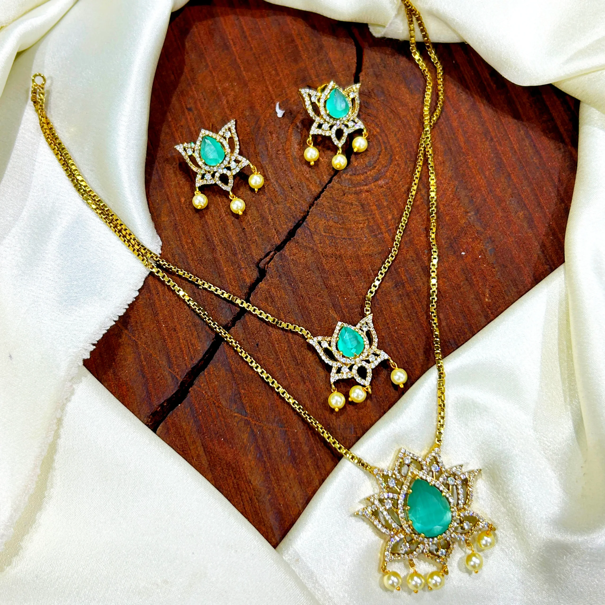 Green stone imitation jewellery set with matching earrings and pendant necklace displayed on a wooden slab with white satin background